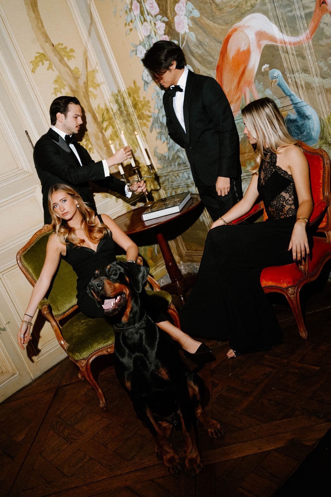Black tie guests in a painted drawing room, around a candelabra