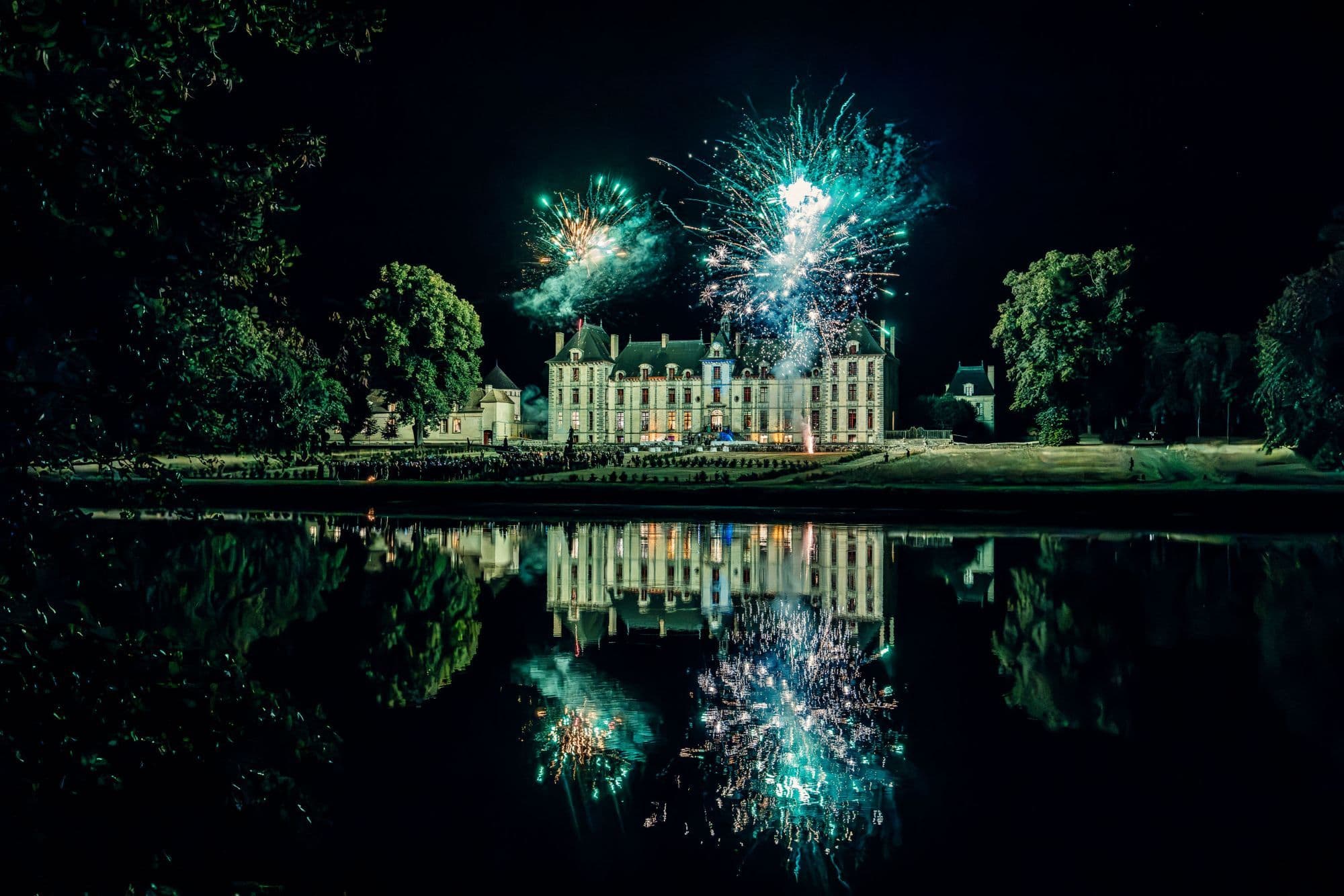 Fireworks above a château, reflected in a lake