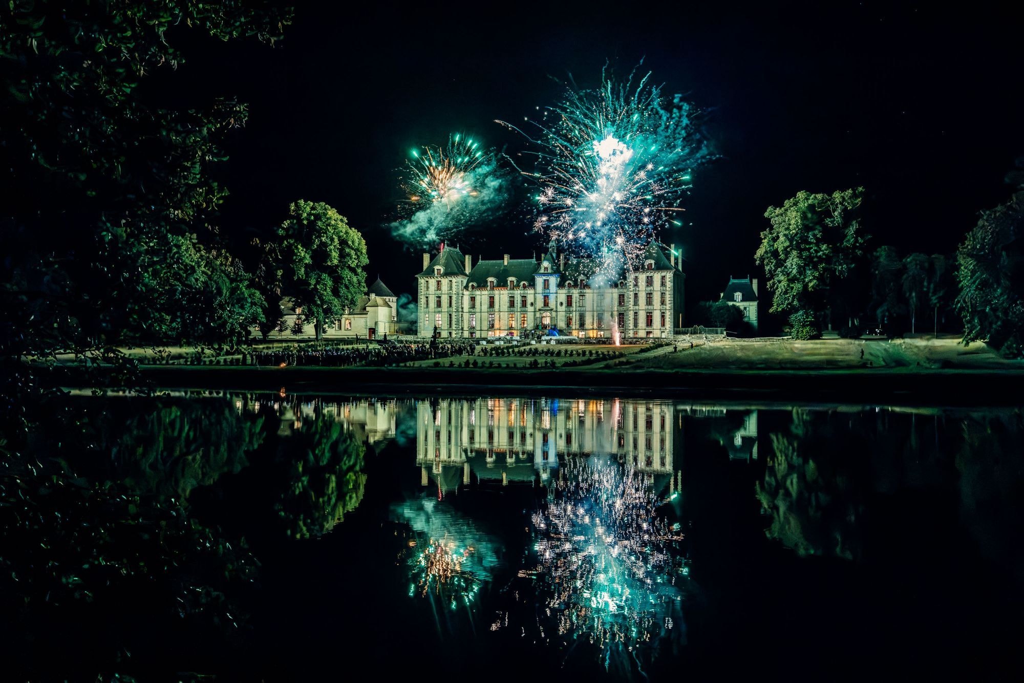 Fireworks above a château, reflected in a lake